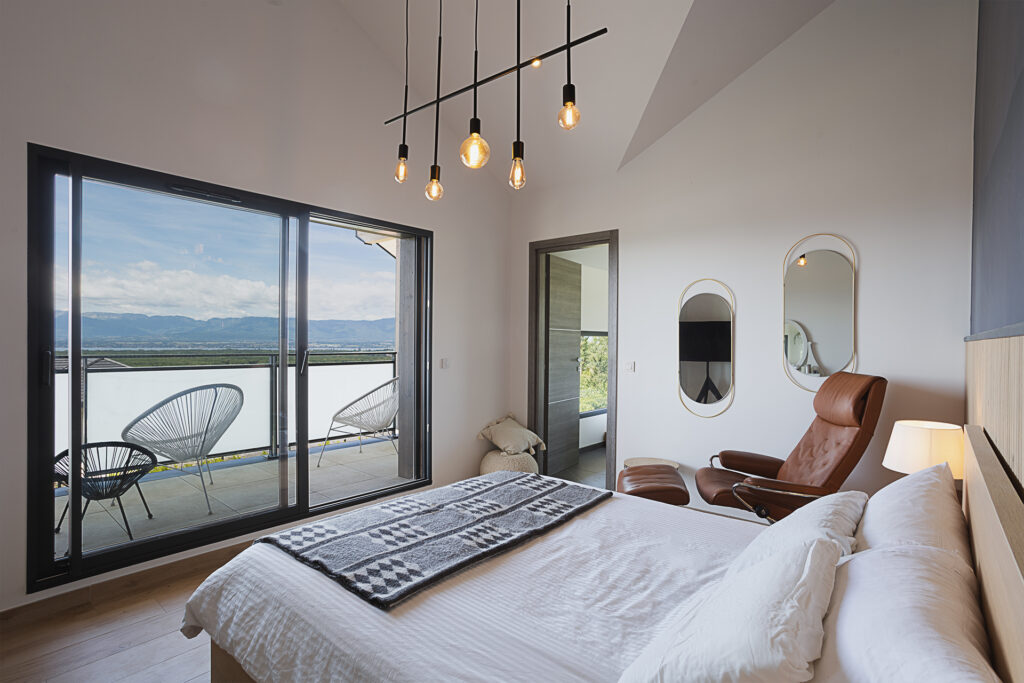 Photographie immobilière en Haute-Savoie. La suite parentale avec une grande baie vitrée donnant sur un balcon avec la vue sur le lac Léman.