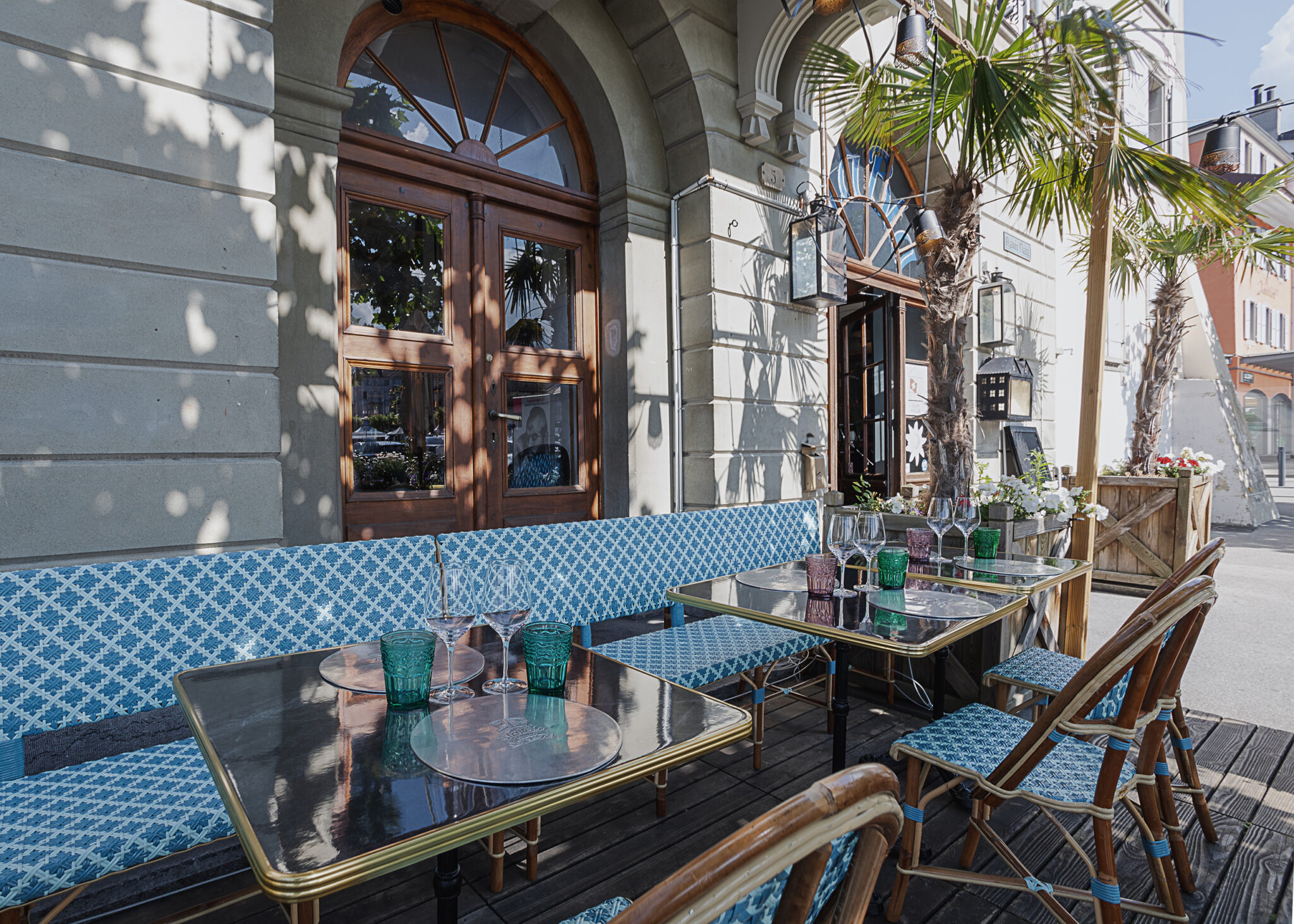 Photographie de la terrasse d'un hôtel-restaurant à Vevey en suisse. La terrasse du restaurant est très fleuri et le mobilier en rotin coloré de blanc et de bleu dans un style balnéaire..